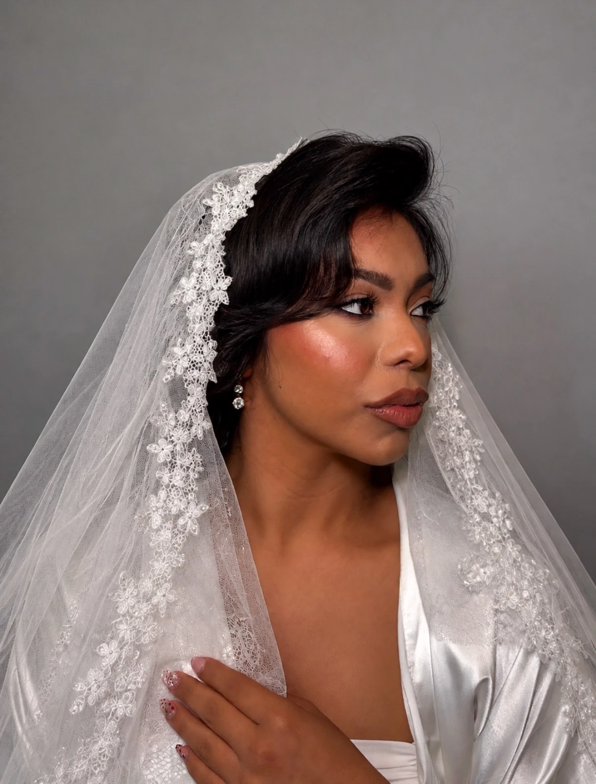 Bride in a lace-trimmed veil with glowing bridal makeup, side profile