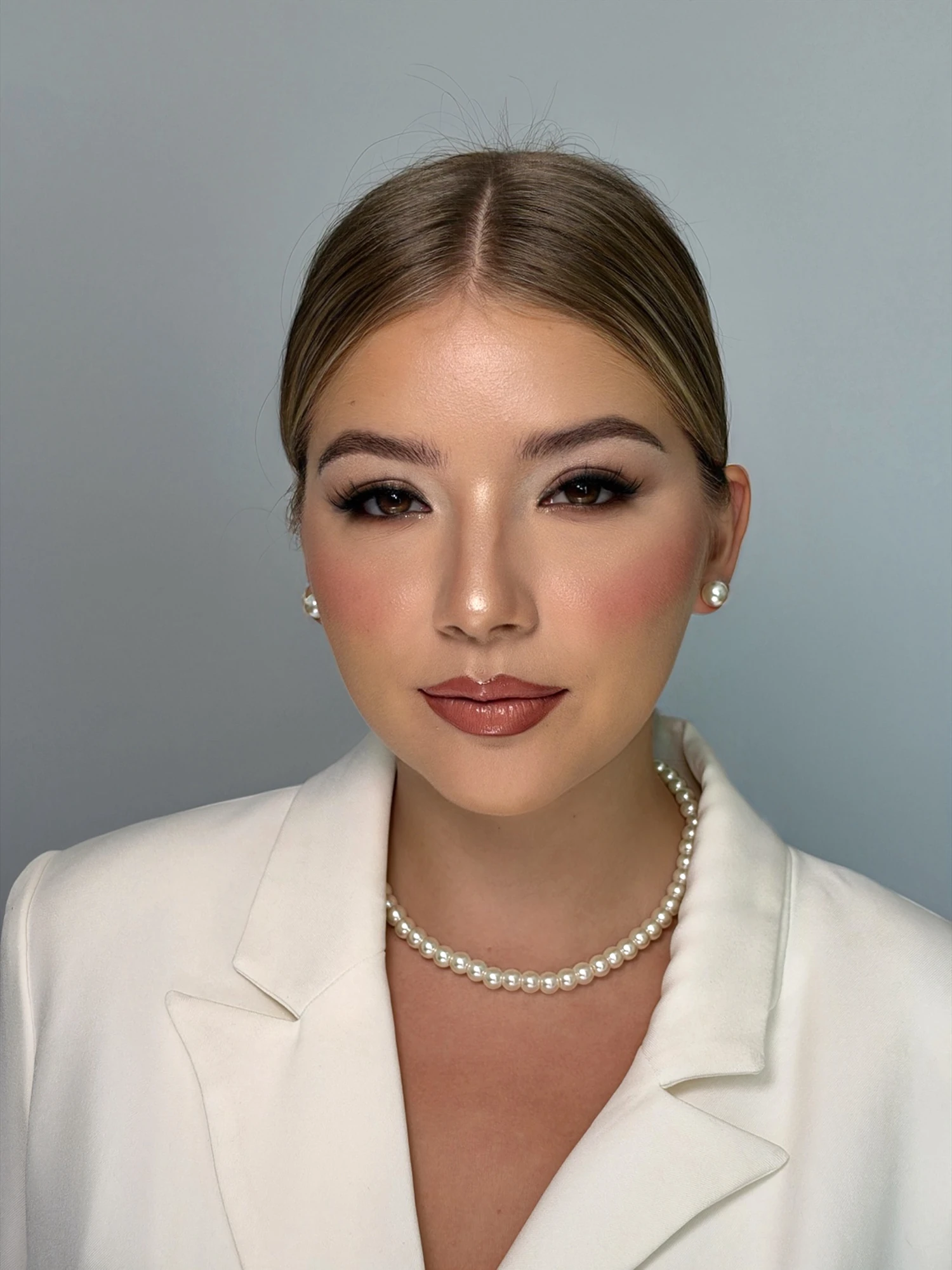 Front-facing soft glam makeup with a brown smoky eye, sculpted cheeks and a pearl necklace