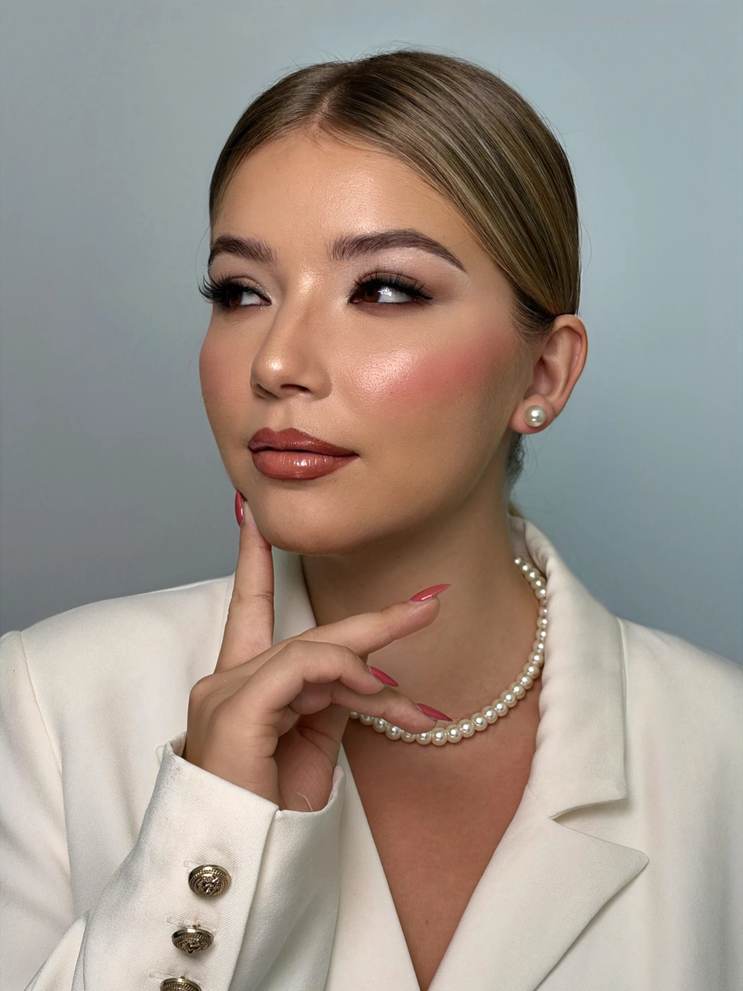 Soft glam makeup with glowing skin, pearls and an ivory blazer, hand at the chin